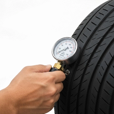 Close-up of a pressure gauge checking a car tire, with a hand holding the gauge against the valve stem, on a clean background.